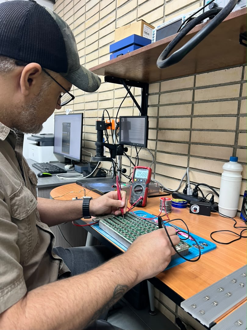 Technician diagnosing an ASIC miner control board with a multimeter at the Astro Solutions bench
