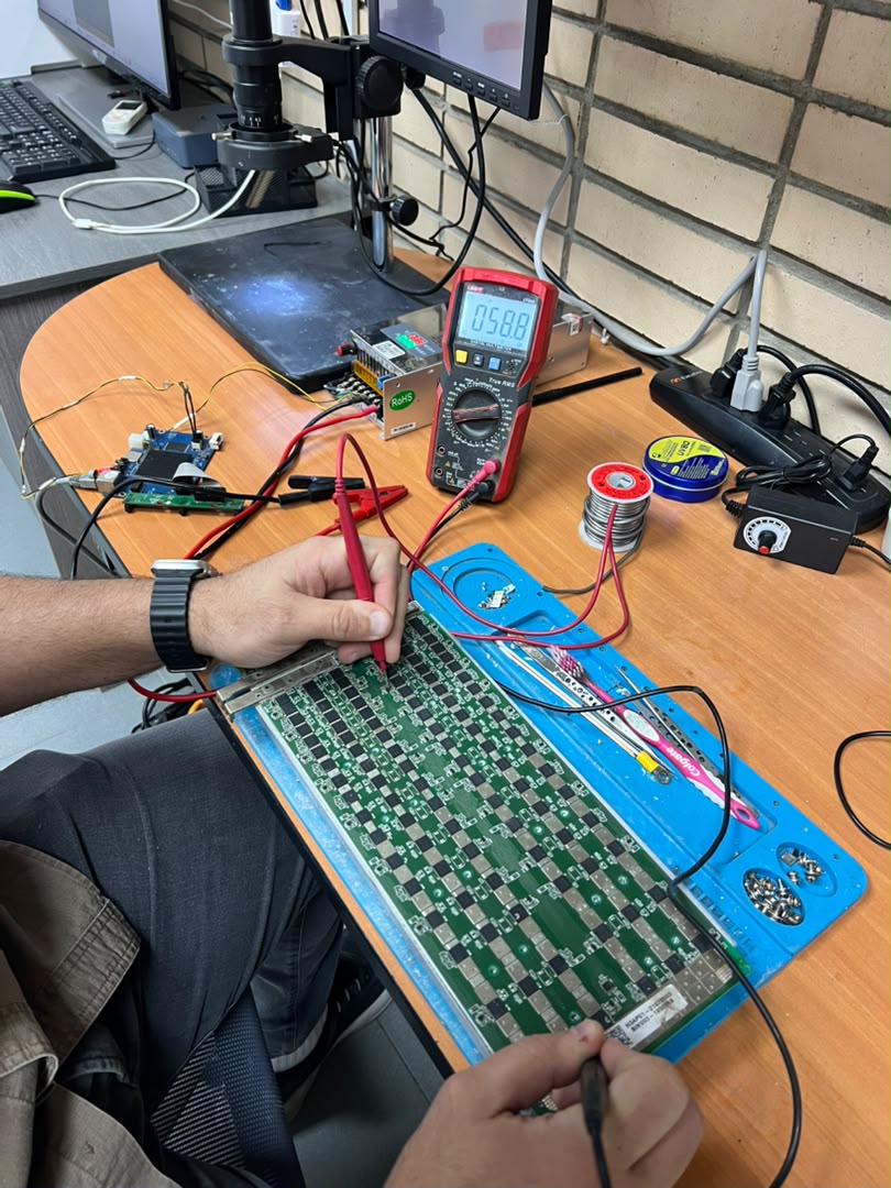 Technician metering an ASIC hashboard at component level with a multimeter on the Astro bench