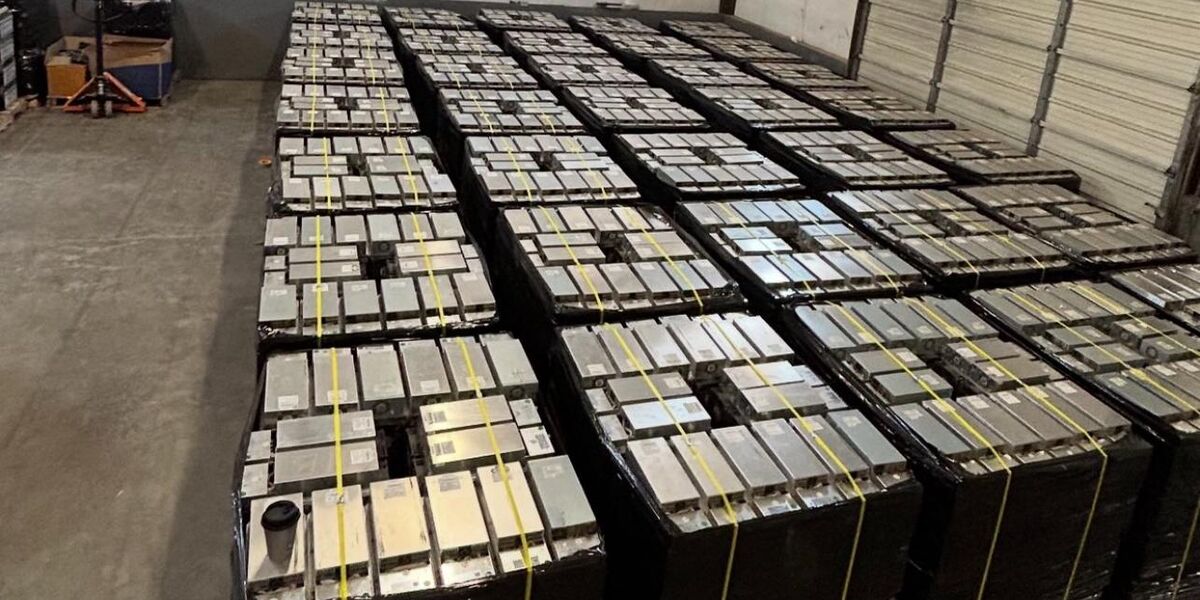 Warehouse floor with rows of palletized, shrink-wrapped ASIC miners ready for shipment